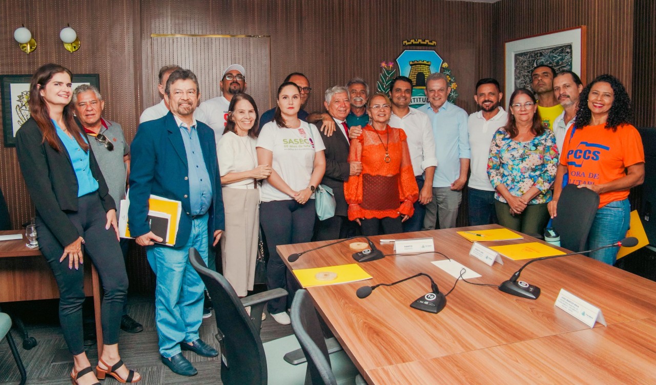 Grupo de pessoas posa para a foto na sala de reunião do paço